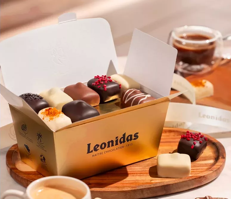 Produktfoto Leonidas Box mit Pralinen auf einem Tisch mit diversen Sorten und zwei Espresso